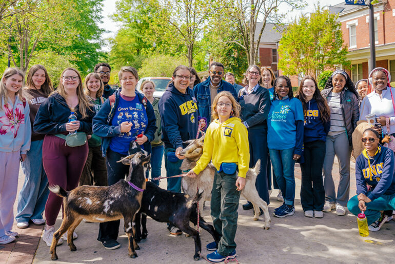 A mix of students, staff, faculty pose with the Chancellor and three goats on College Ave.