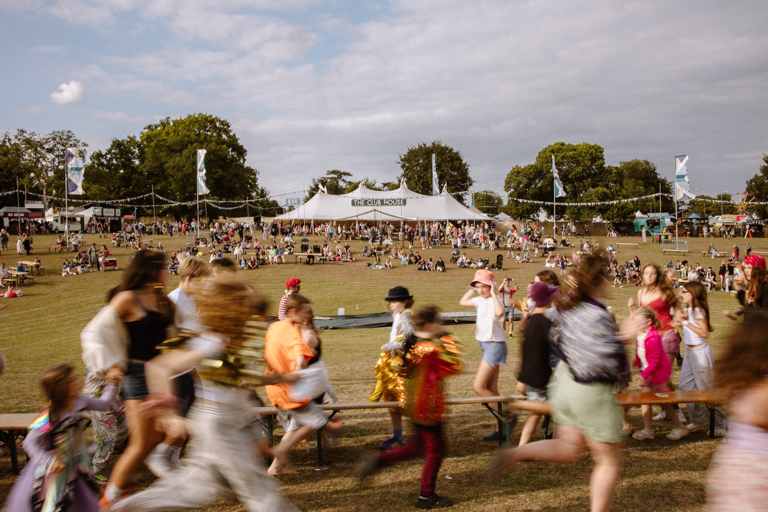 A field in the summer with people dancing and a stage in the distance.