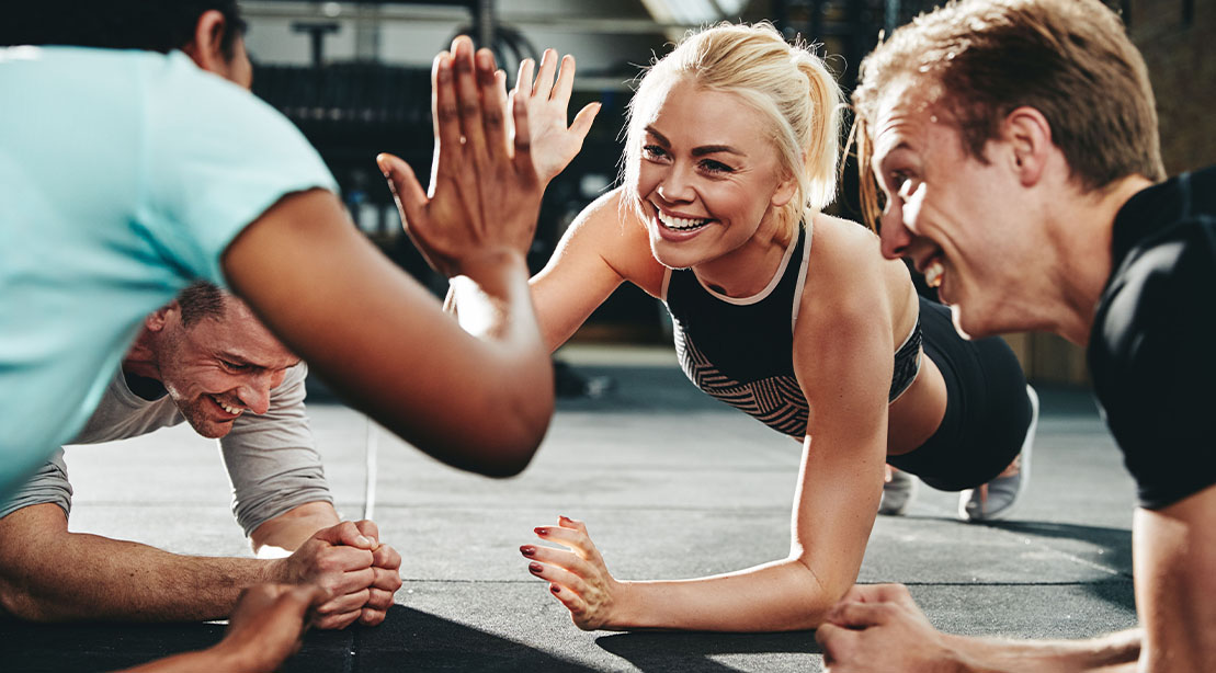 Young fit athletic group high fiving each other while performing planks