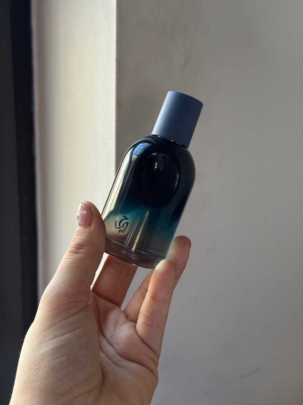 Fragrance bottle held in hand against a light background.