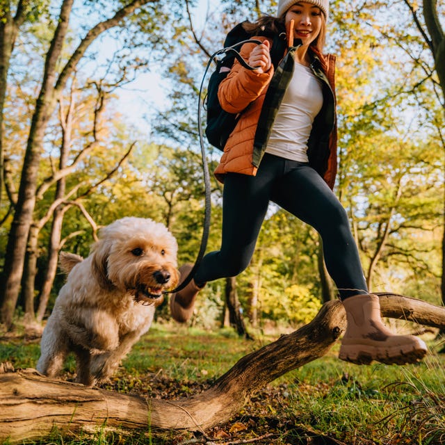 Young woman jumping over wooden trunk with her dog while exploring nature