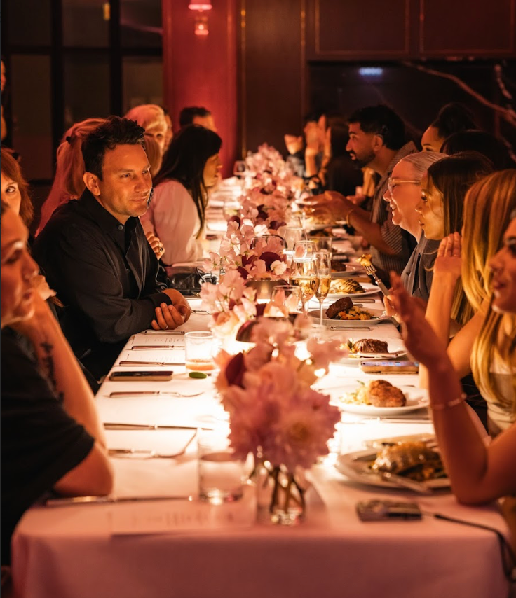 Long dining table set for a formal meal with guests engaged in conversation.