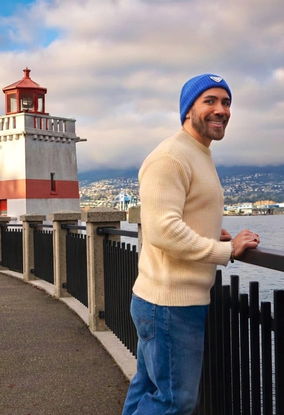 Man leaning on a railing near a waterfront with a lighthouse in the background.