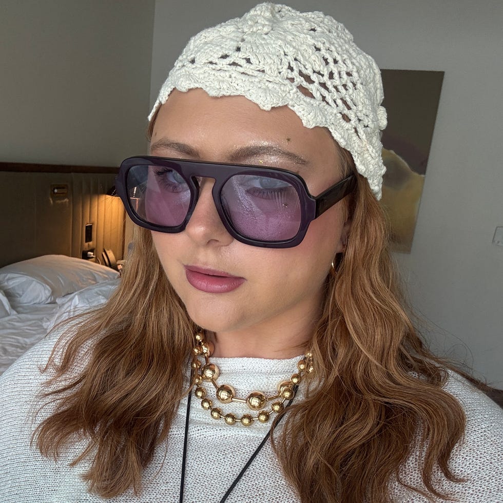 A person dressed in a white cover-up, sunglasses, and jewelry in a hotel room.