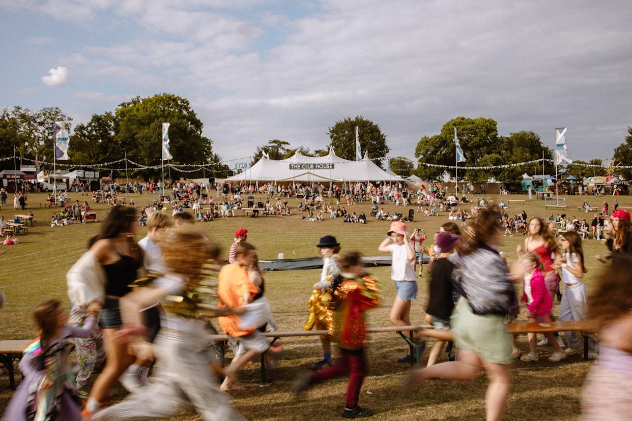 A field in the summer with people dancing and a stage in the distance.