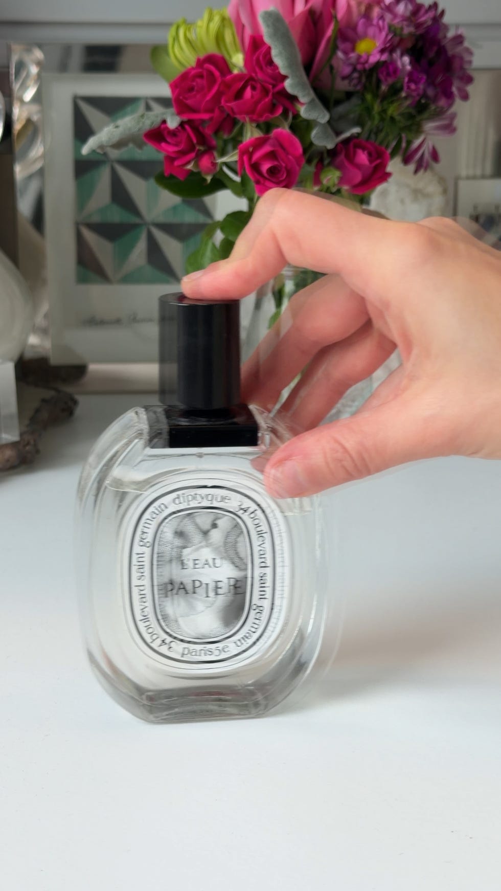 Scented perfume bottle being held near a bouquet of flowers.