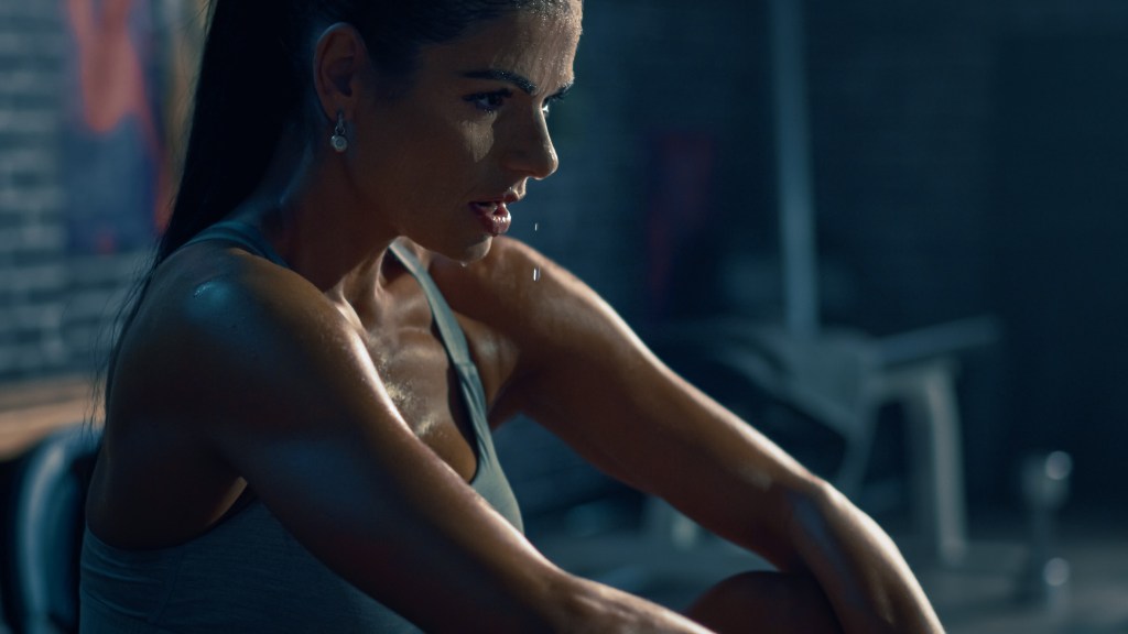 A perspiring female athlete in a gym catching her breath after an intense workout.