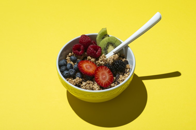 Bowl with muesli ,chocolate and fruits on on yellow background