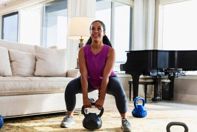 an adult black woman in her 30s exercising with kettlebells at home in the living room