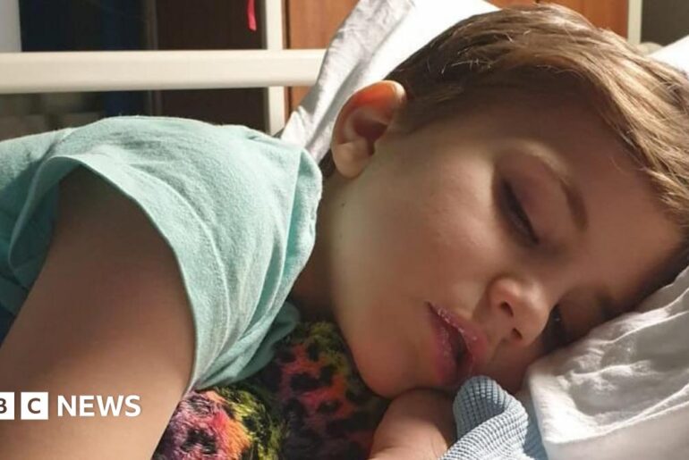 Roo - A young child sleeping on a hospital bed, lying on his side with his head on a pillow and holding a soft toy.