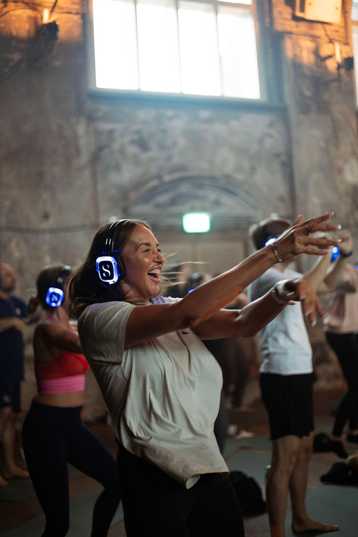 A young, animated woman dancing to music with headphones in a group of festival-goers.