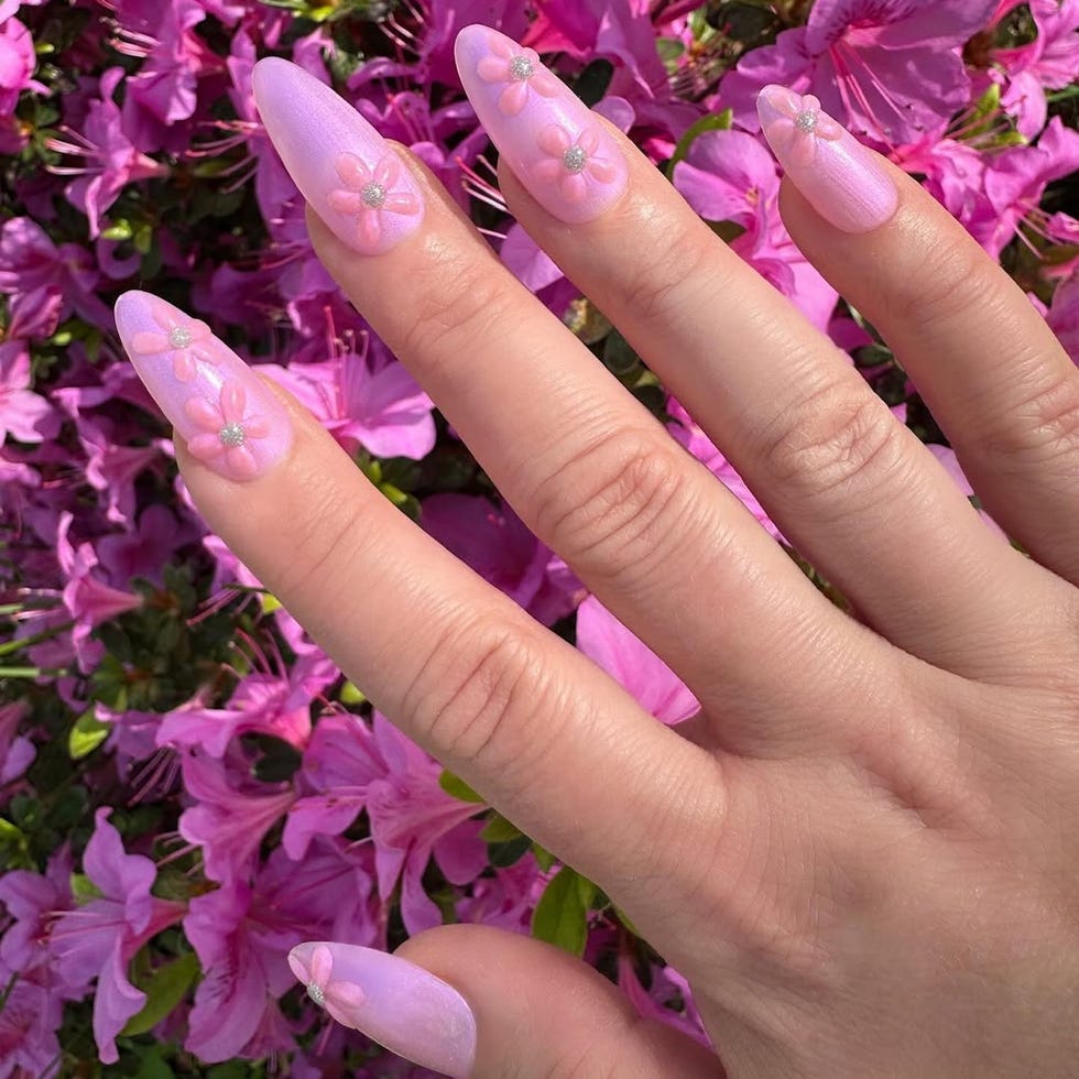 Decorative long nails with floral designs in front of pink flowers.
