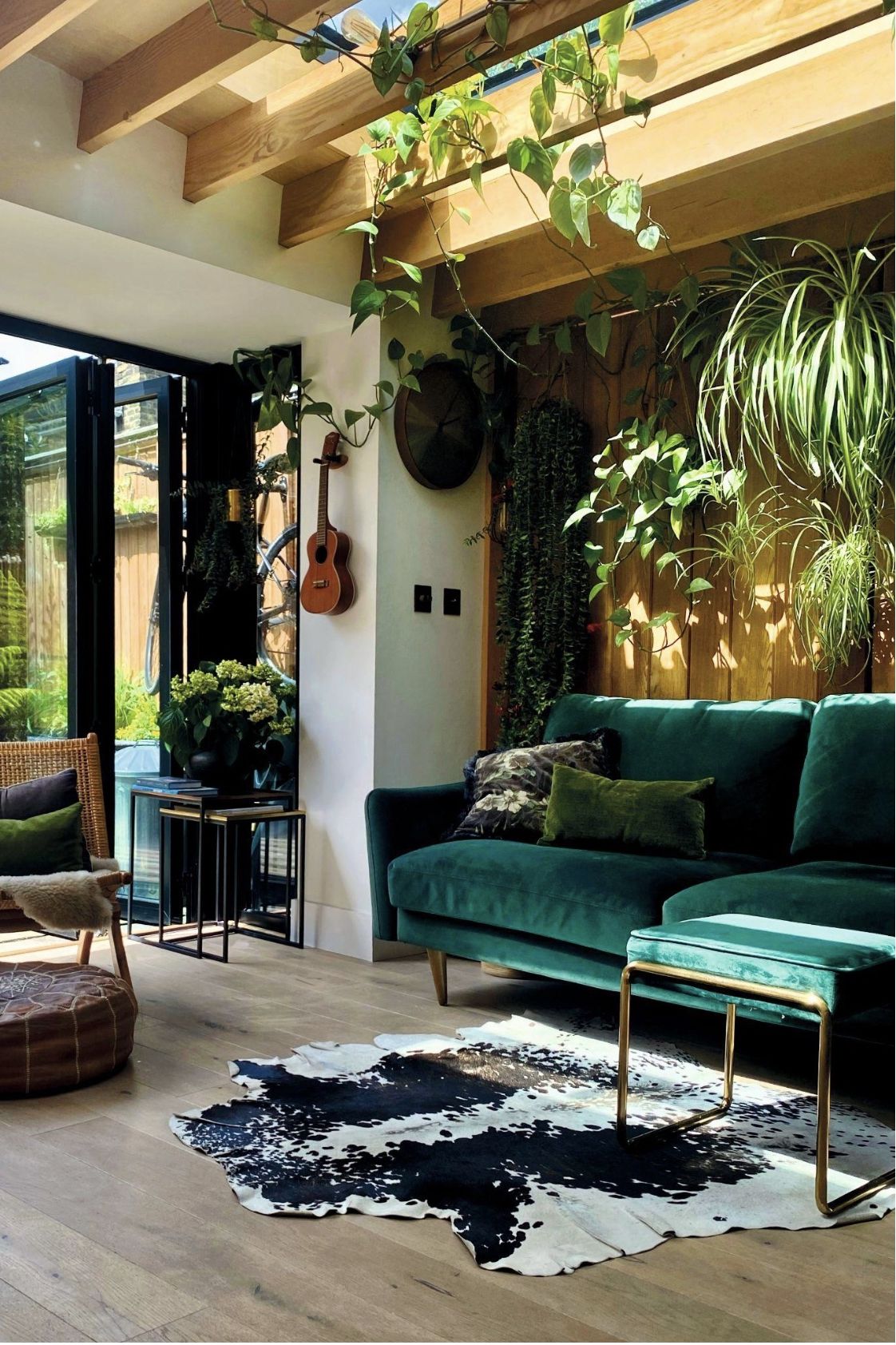 a living room with a green sofa, cow hide rug, lots of plants and views to the garden