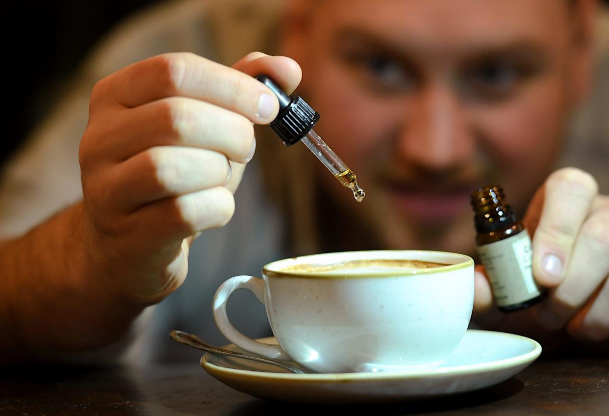 A man squirts a tincture of CBD oil on a cappuccino.