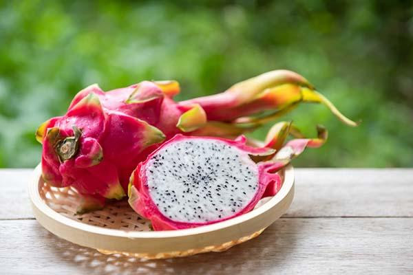 A whole dragon fruit and half of another with the inner speckled flesh facing up, placed on a small wicker dish.