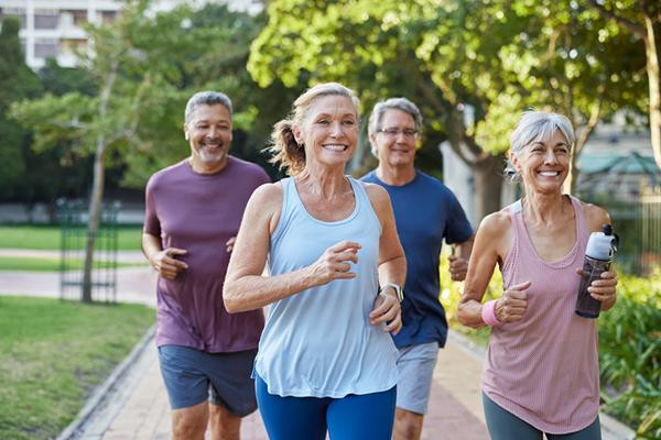 A group of four mature adults jogging in a suburban park setting.