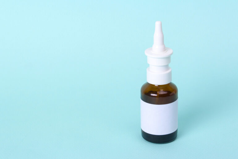 Nasal spray for cure cold. Glass bottle with medicine on a green background. Copy space for text