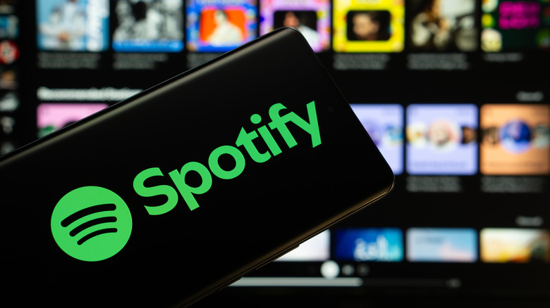 The Spotify logo on a smartphone with the Spotify app open in the background on a computer.
