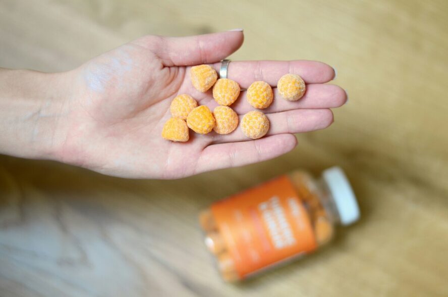 Image of an open palm with a handful of orange gummy vitamins, floating above the bottle.