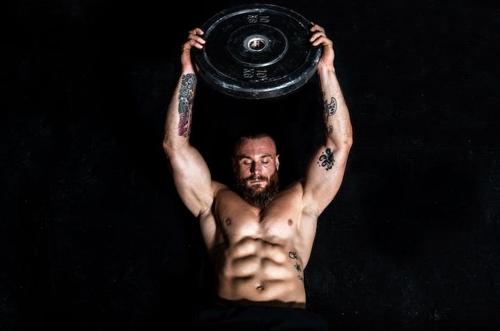 young sweaty fit strong muscular man with big muscles doing hardcore cross abs workout training on the gym floor with weight plate
