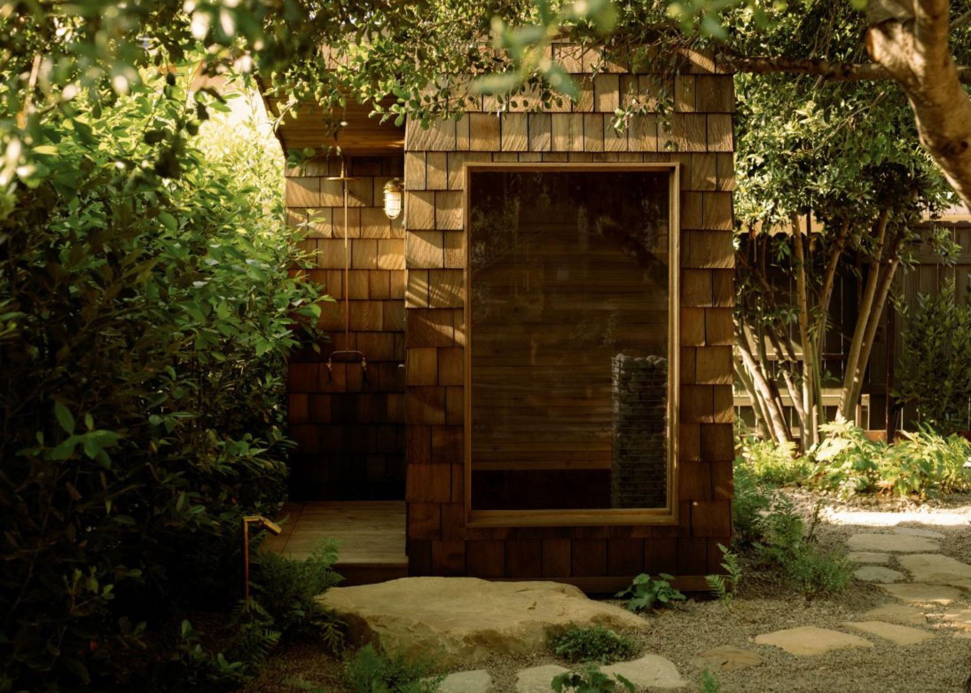 sauna with a shower in a pebble stone garden surrounded by foliage and greenery