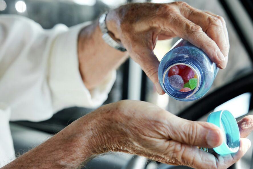 Image of an elderly woman's hand pouring a bottle of gummy vitamin supplements into her other palm.