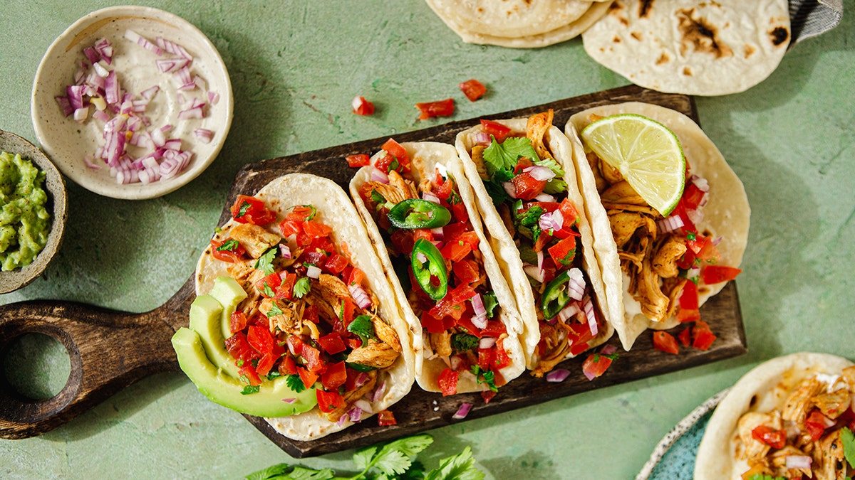 A plate with several tacos filled with meat and garnished with cilantro and onions.