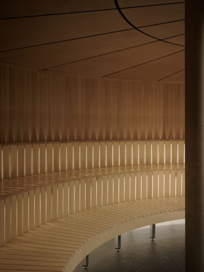 Curved wooden bench seating with vertical slats and soft, indirect lighting in a modern, minimalist interior space.