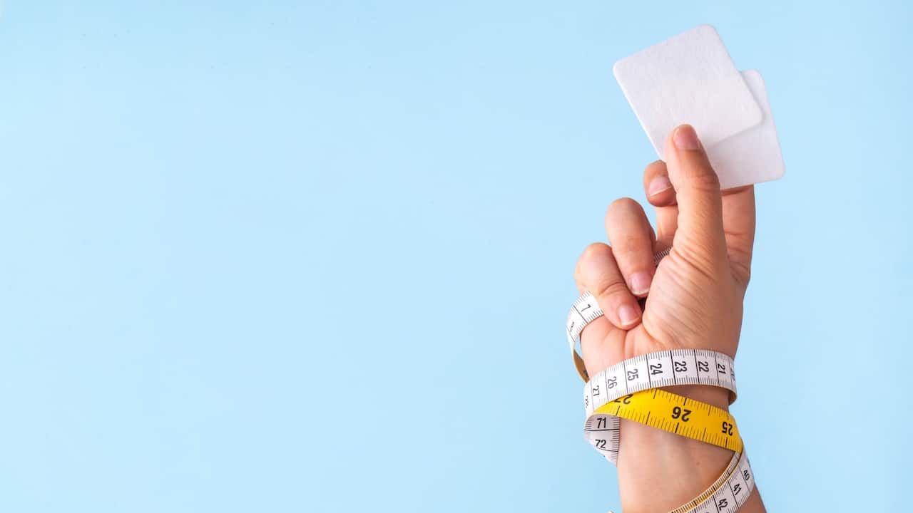 Slim patches with measuring tape and woman hand on blue background