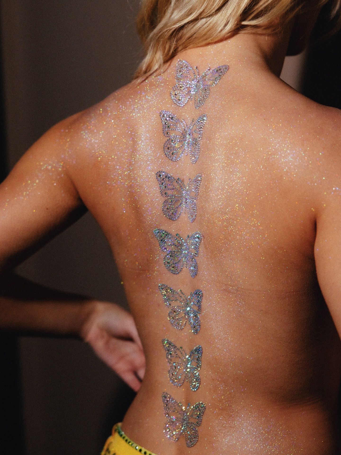 A photo of Sophia Sinot's back covered in body glitter and her spine lined with  rhinestonestudded butterfly back tattoos.