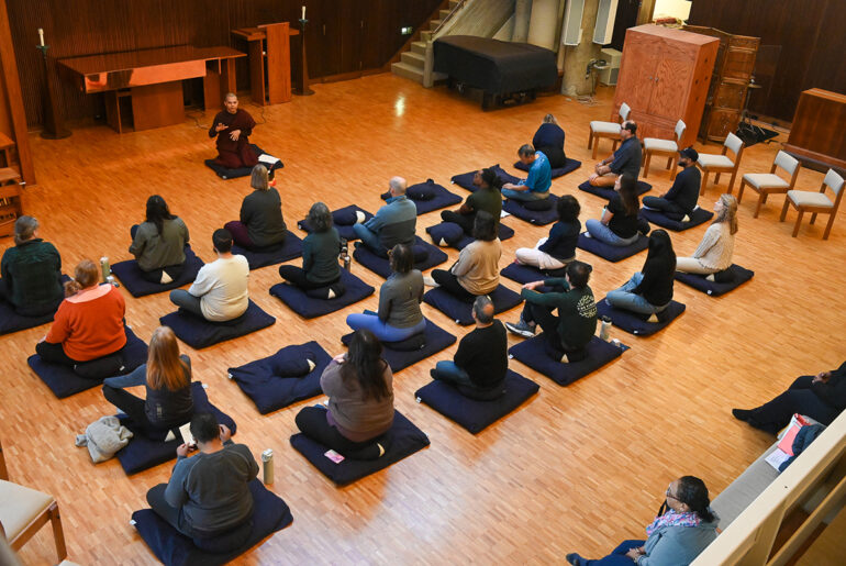 group of participants sit cross-legged on yoga mats in Cannon Chapel, with a monk at the front of the room