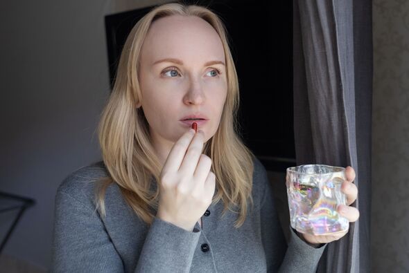 Woman taking iron supplement capsule with glass of water. Female health care, iron deficiency anemia treatment, vitamins and minerals intake for welln