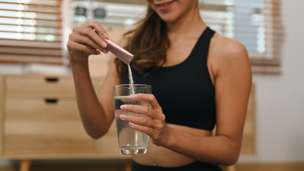 A woman pouring collagen powder from a packet into a glass of water.