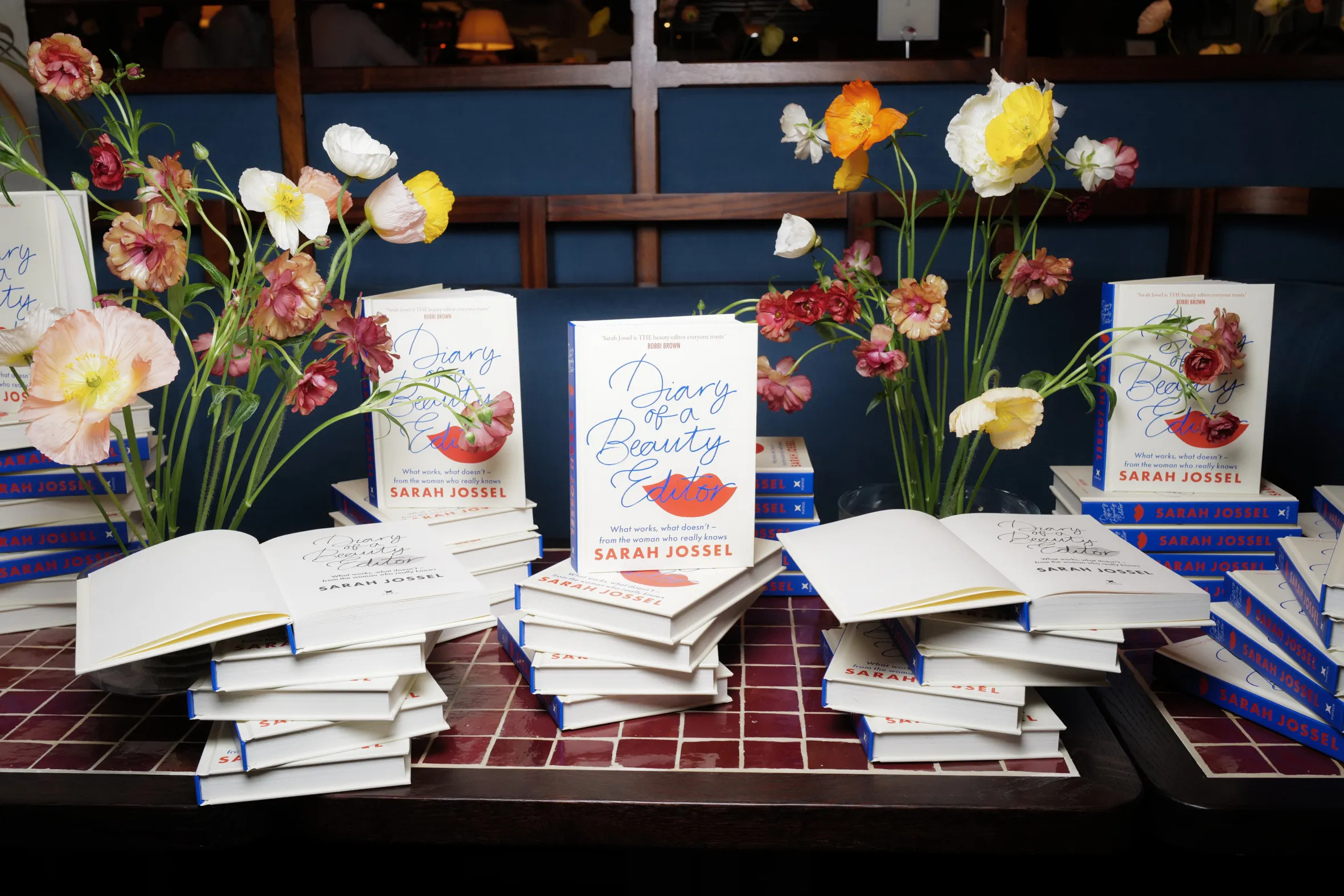 Copies of Sarah Jossel's book "Diary of a Beauty Editor" on display with floral arrangements.