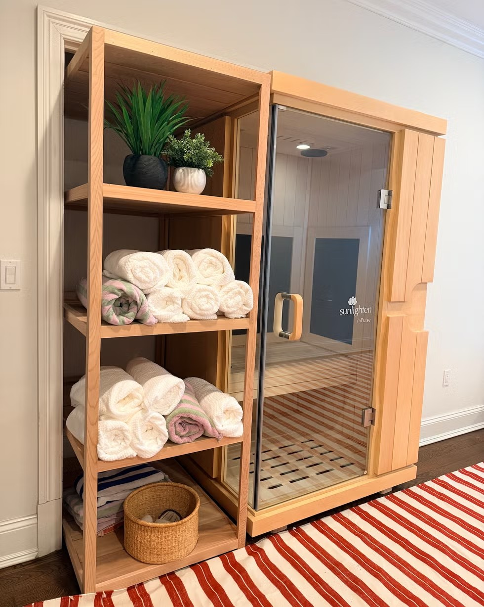 Wooden shelving unit with towels and potted plants next to a glass-fronted sauna.