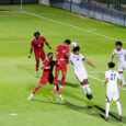 Two competing men's soccer players jump and hit a ball with their heads.