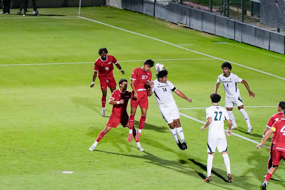 Two competing men's soccer players jump and hit a ball with their heads.