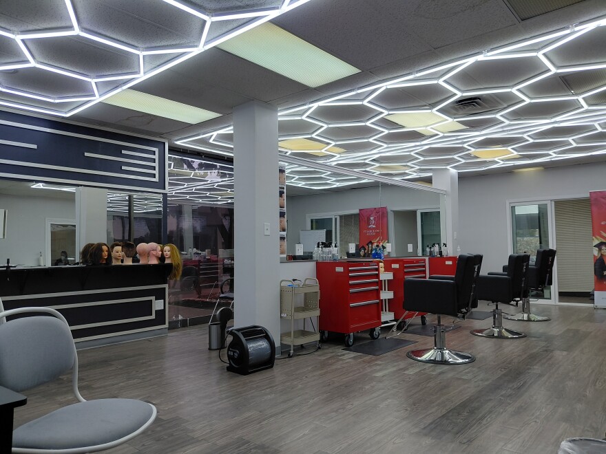 A beauty salon with red files and black chairs. There are mirrors all around the wall and mannequin heads. 