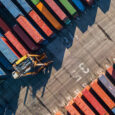Aerial view of container port, just showing the dock with containers and a forklift.