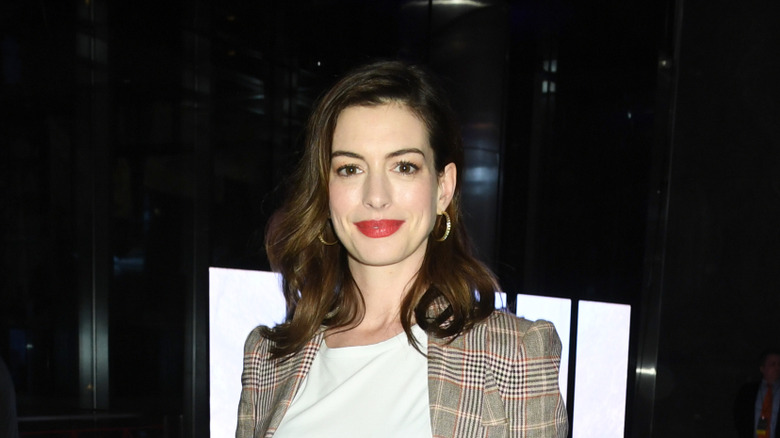Anne Hathaway posing in a plaid blazer with red lips in 2019.