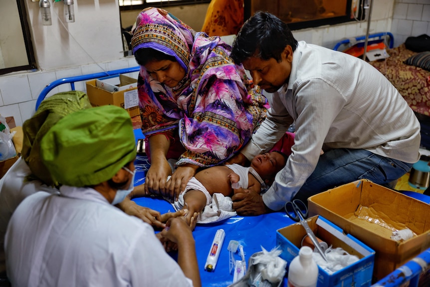 Three adults pin down a small child to treat the child for measles.