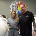 Janelle and Cory Ardizzone standing in front of a hyperbaric oxygen chamber.