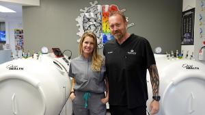 Janelle and Cory Ardizzone standing in front of a hyperbaric oxygen chamber.