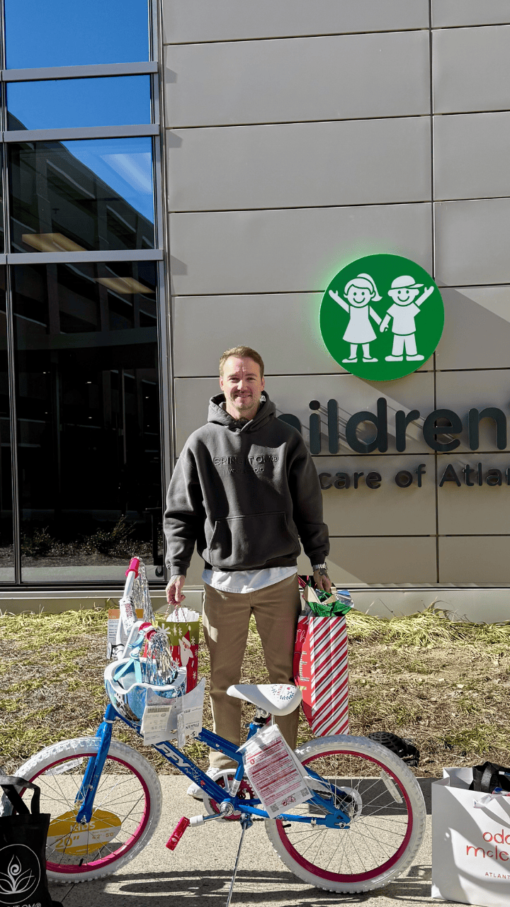 Man standing outside a children's care center holding gift bags next to a decorated bicycle.