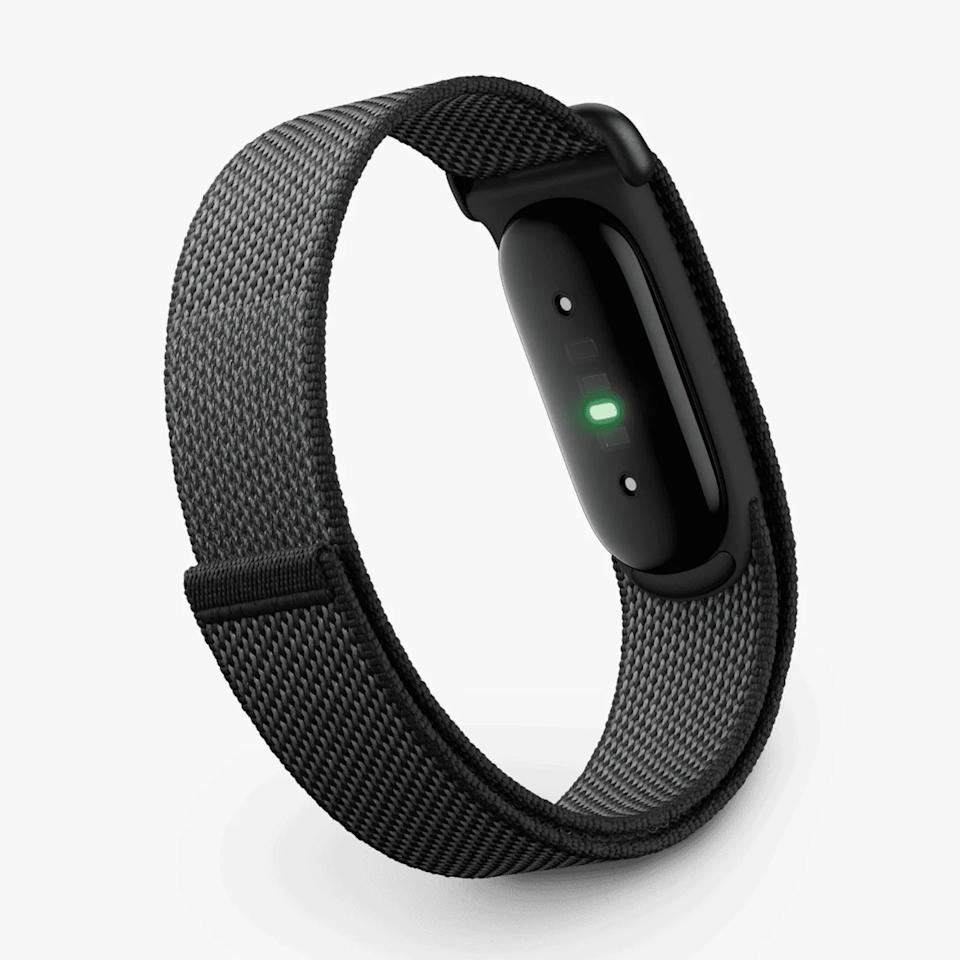 Black fitness tracker with green sensor light and woven nylon strap on a white background.