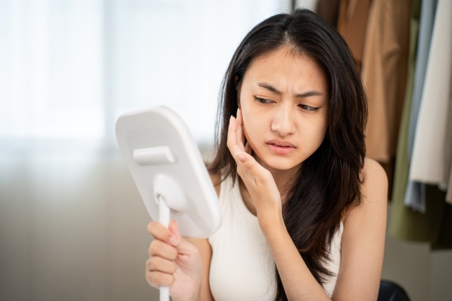 Worried woman looking at mirror, touching dry irritated skin