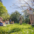 A group of college age students performing a play in a garden in front of kids
