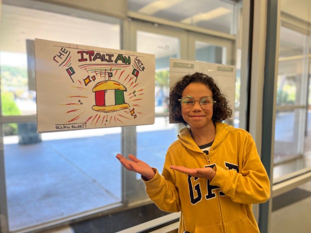 Sixth-grade student, Ricky Nutt, poses with the poster he made to promote his group's newest culinary creation. The "Italian Special" is a chicken sandwich with pesto aioli, now offered district-wide. (Photo by Sarah Rodriguez)