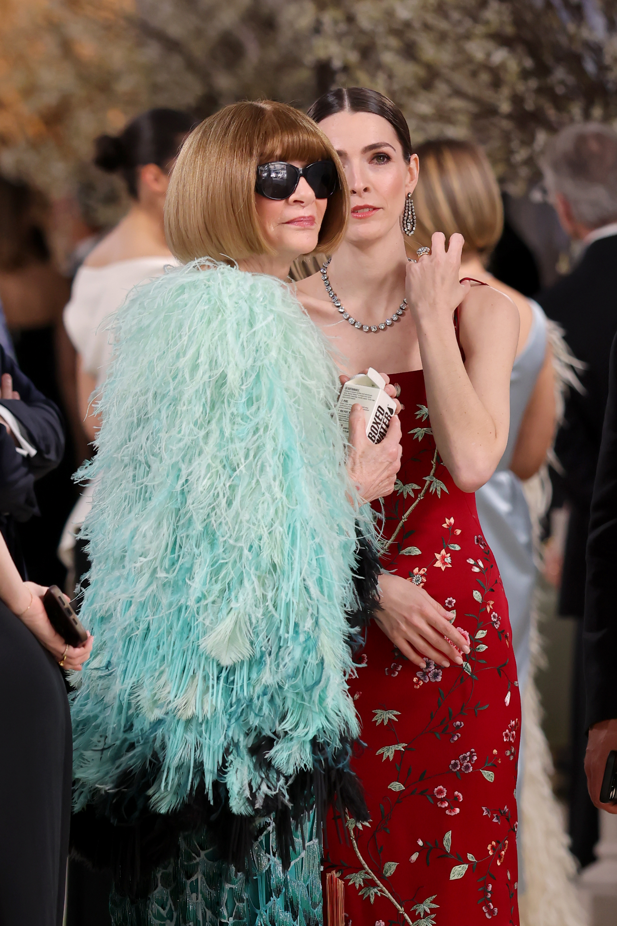a woman in a blue feather cape next to a woman in a red dress with dark hair