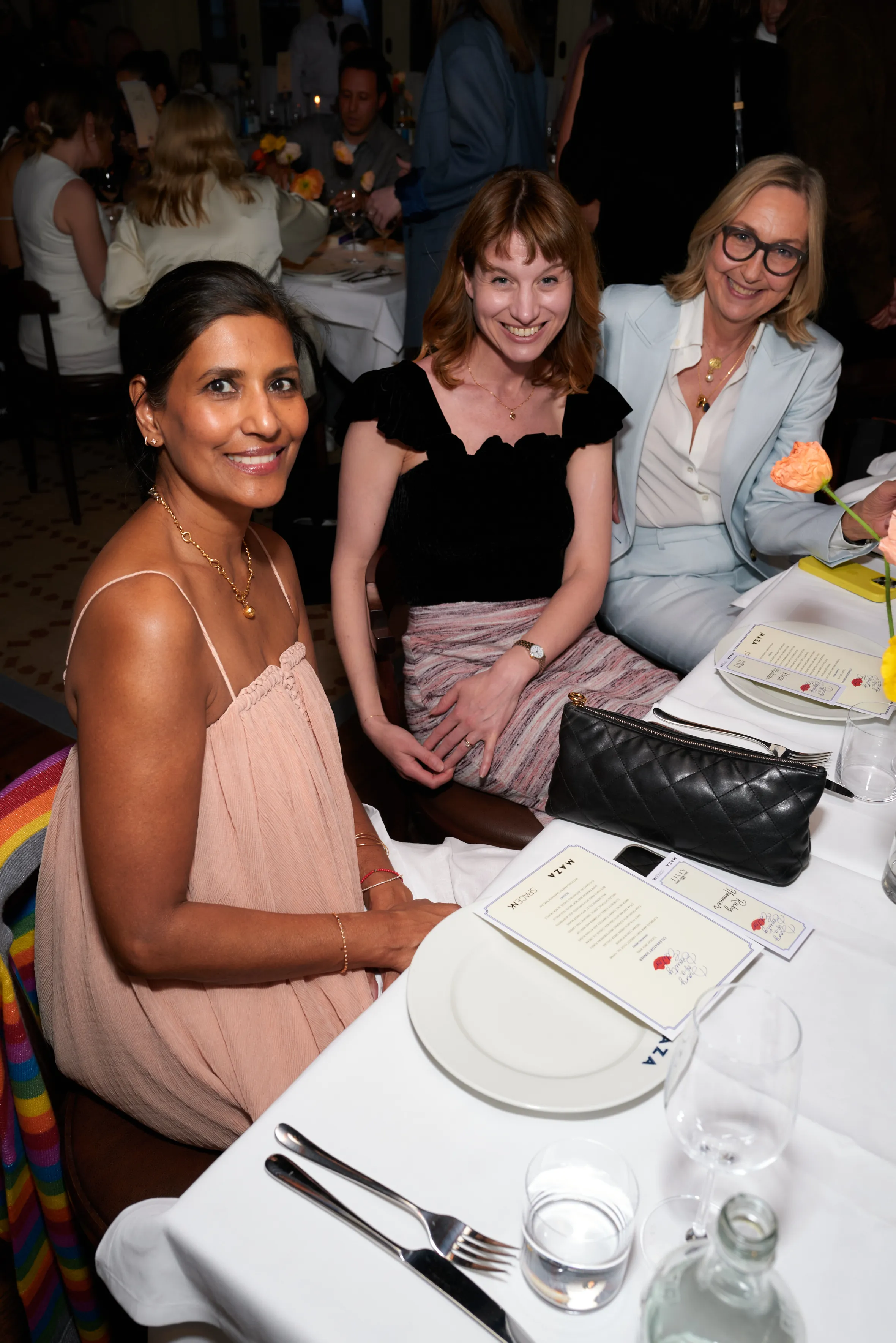 Three women sitting at a dinner table, smiling at the camera.